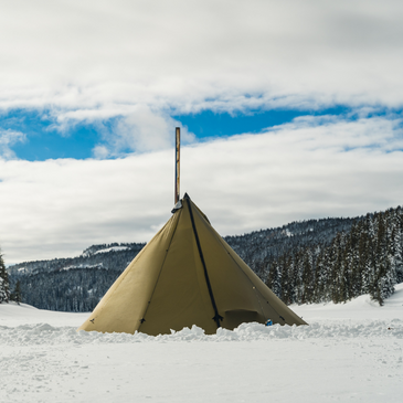 Seek Outside teepee pitched on compact snow with twisted stakes holding guy lines, vast alpine mountains in the background