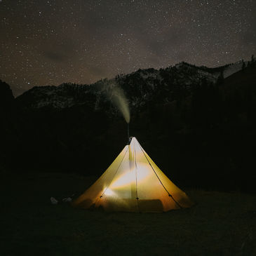 8 person tipi at night, glowing from light within as smoke curls out of the stove pipe