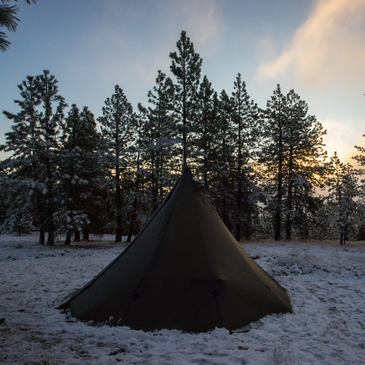 Sunny morning at backcountry tipi camp with stove pipe visible and gear tracks in snow around the 13-foot diameter shelter