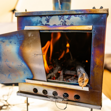 Titanium wood stove with firebox glowing from active fire and heat radiating from titanium panels