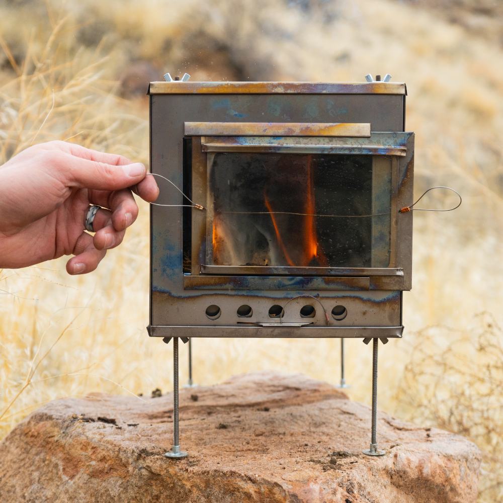 Tent stove with glass door showing bright orange flames and glowing embers inside the firebox