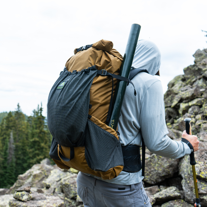Hiker climbs a rocky slope with a loaded Flight 3 backpack with front stretch pocket visible
