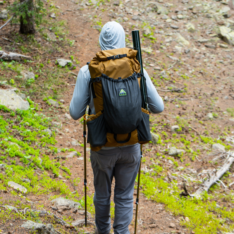 Backpacker with a full Flight 3 pack and side water bottle pockets, walking a ridgeline trail.