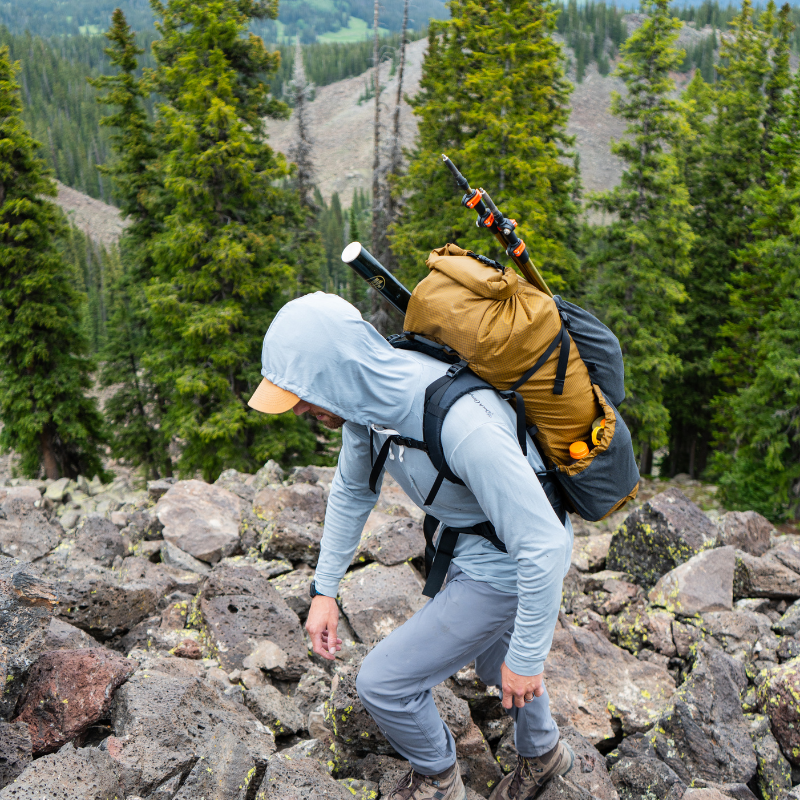 Hiker scrambling up a rocky trail with a Seek Outside Flight 3 backpack, showing the pack's body-hugging fit for agile movement.