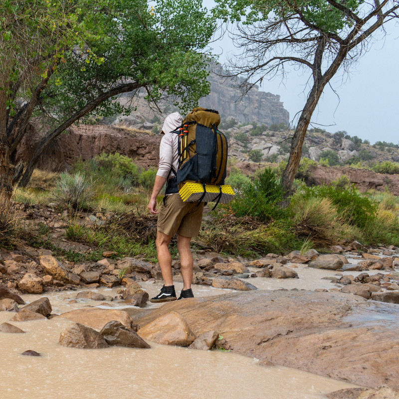 Backpacker with Divide 4800 crossing muddy stream, packbag highly water resistant, side water bottle pockets holding two trekking poles