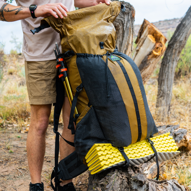 person adjusts the roll-top closure of Divide backpack