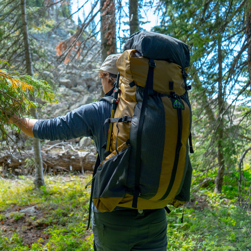 Backpacker trekking through green forest with a Divide 4800ci hiking pack