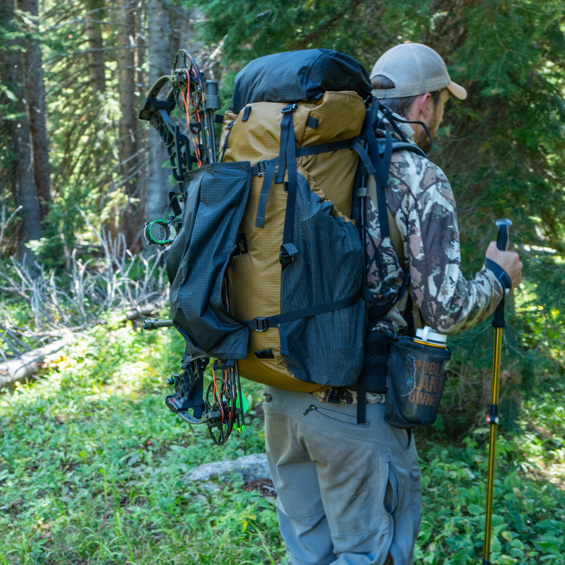 a man wears a goshawk backpack in a dense forest; the detachable talon on the backpack is used to attach a crossbow to the backpack
