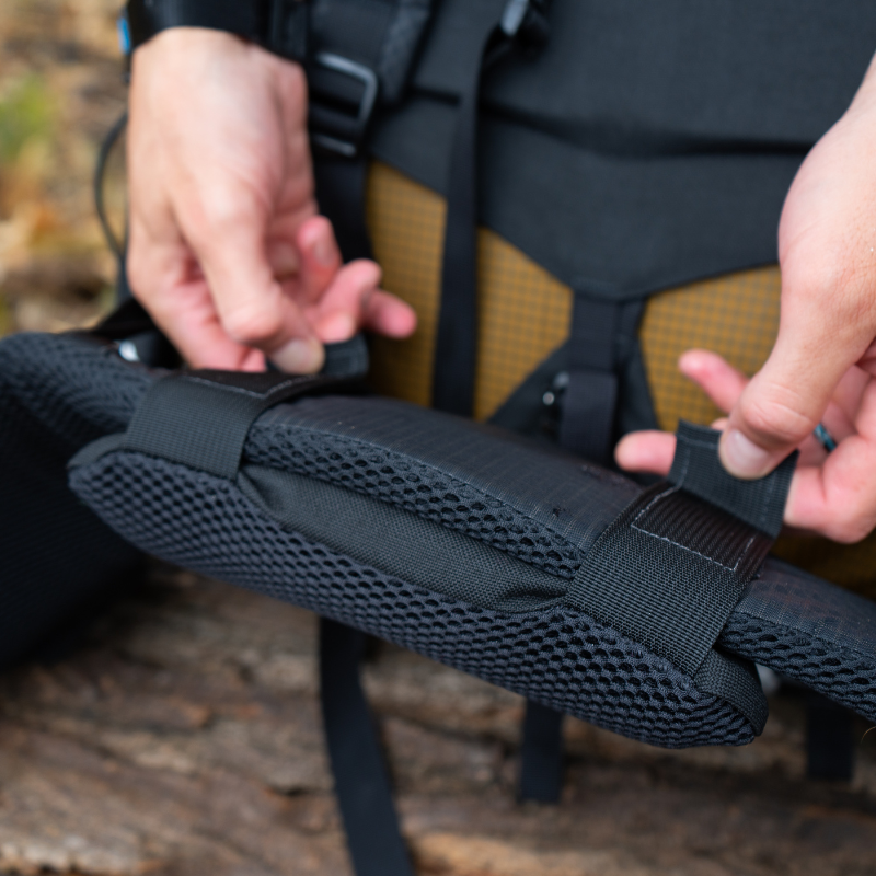 a man connects a lumbar pad to the hipbelt of a Seek Outside backpack