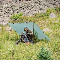man uses Gunnison Lightweight backpacking tarp as a glassing shelter on a grassy hillside