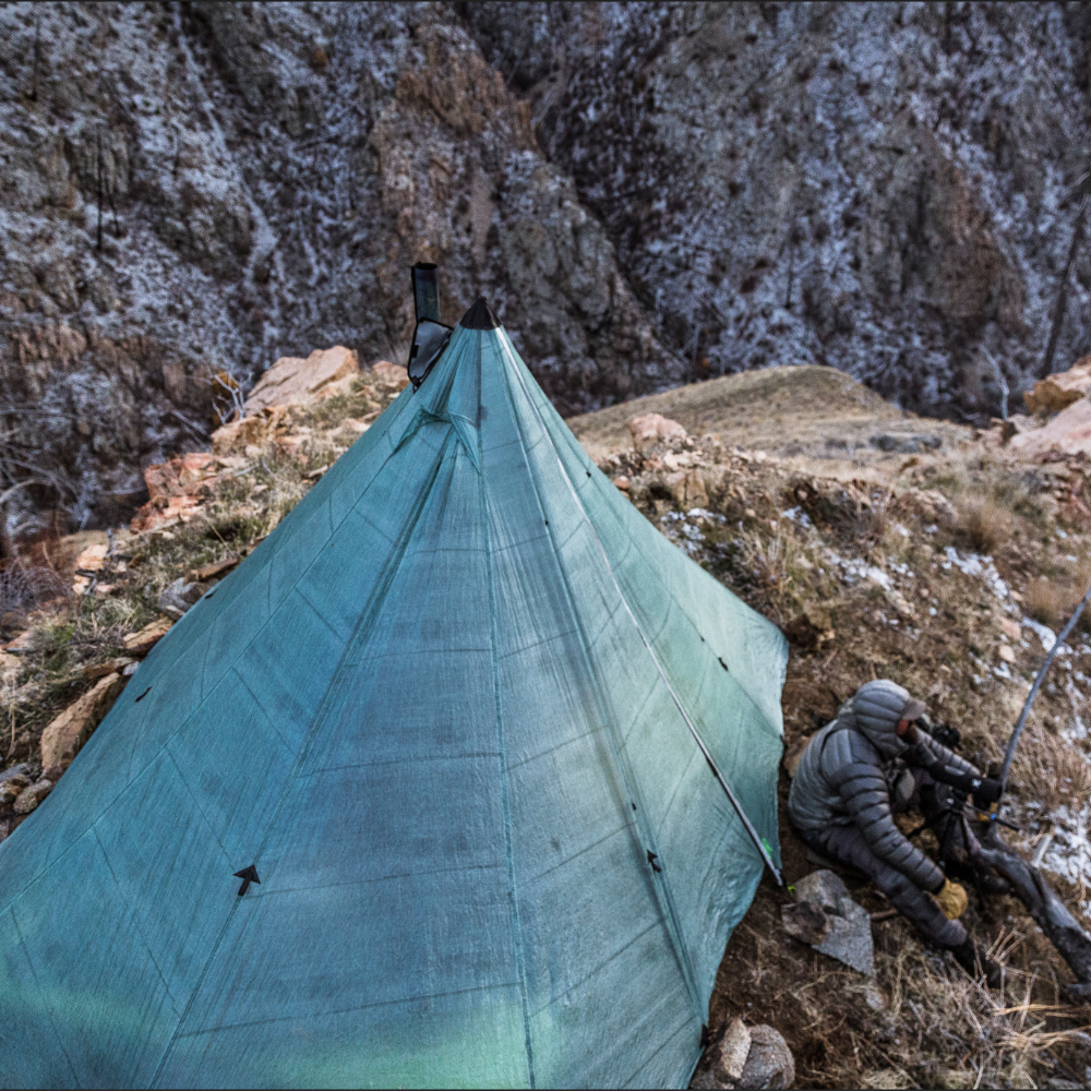 a man sits outside a Redcliff 6p Ultralight Dyneema With Stove Jack set up on a rocky cliffside