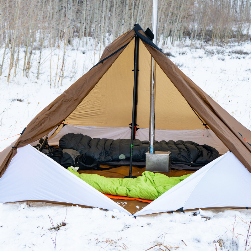 Interior of a cimmaron tent with floor/liner system installed inside, two sleeping bags, a wood burning stove and gear inside