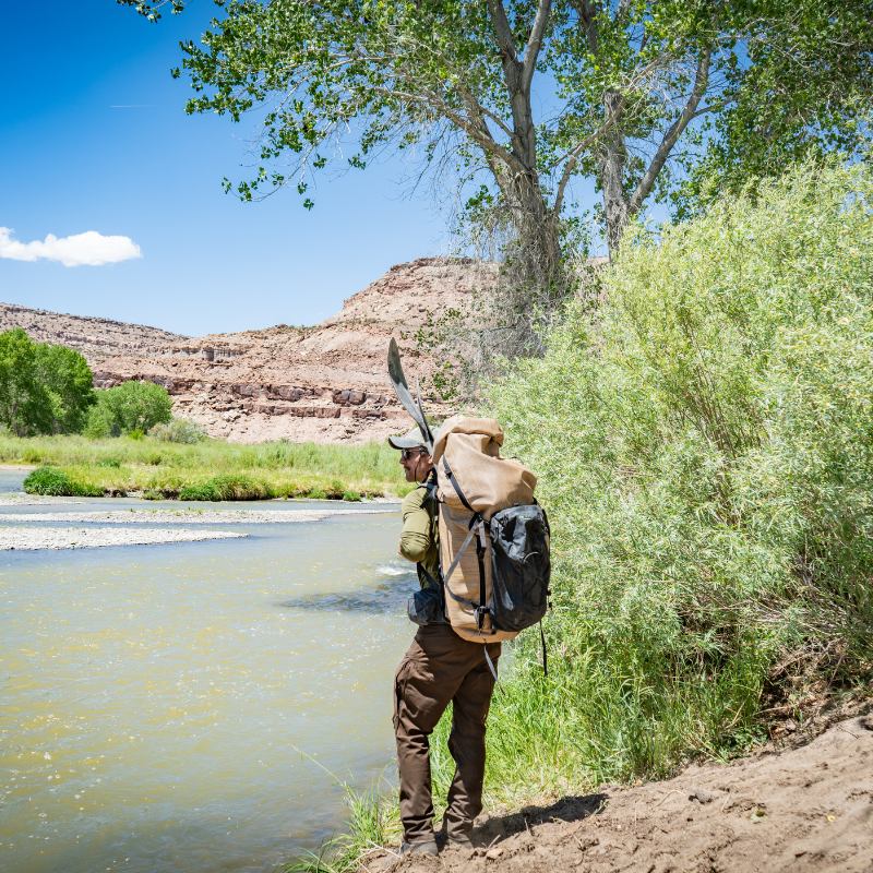 a man stands on a river bank with a Wetlands backpack on