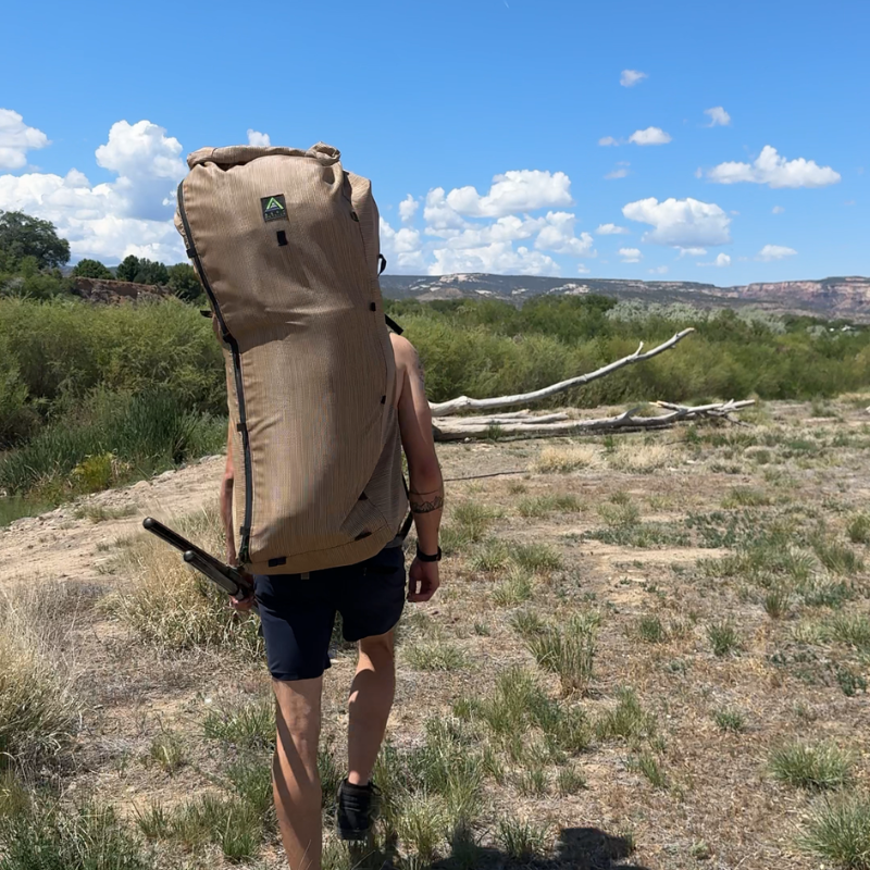 a man walks through a dirt clearing wearing a Wetlands backpack