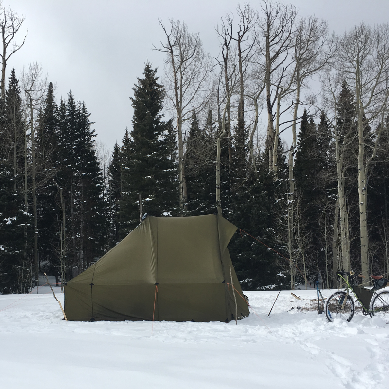side view of a Courthouse wall tent in a snow covered forest surrounded by tall trees in a winter setting