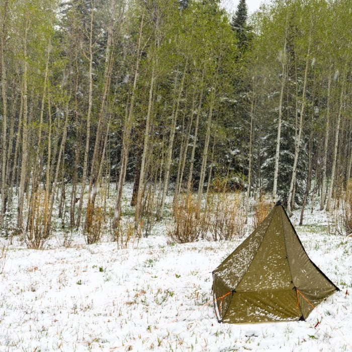 a Brightwater tent set up in a snowy field, trees in the background have bright green spring leaves budding