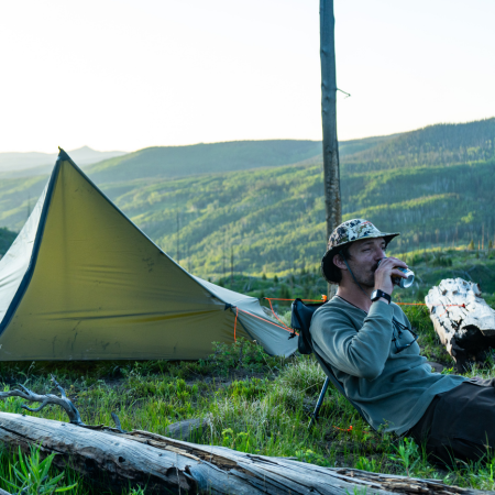 camping site with a tent set up, person sits in a sitting saddle looking out over a grassy hillside