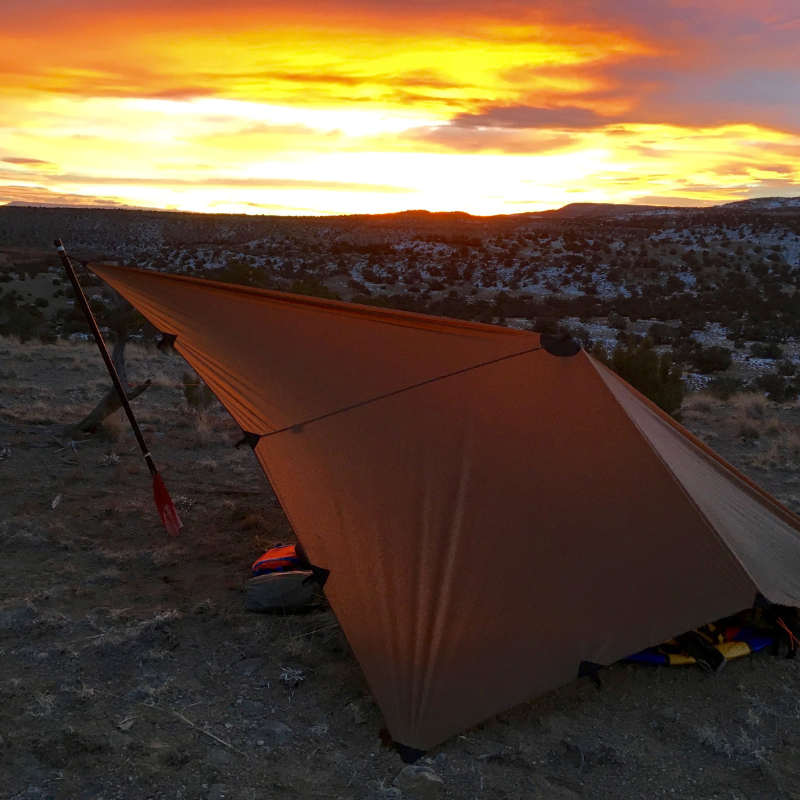 DST tarp set up up with boat oar, snow covered bushes and sunset in the background