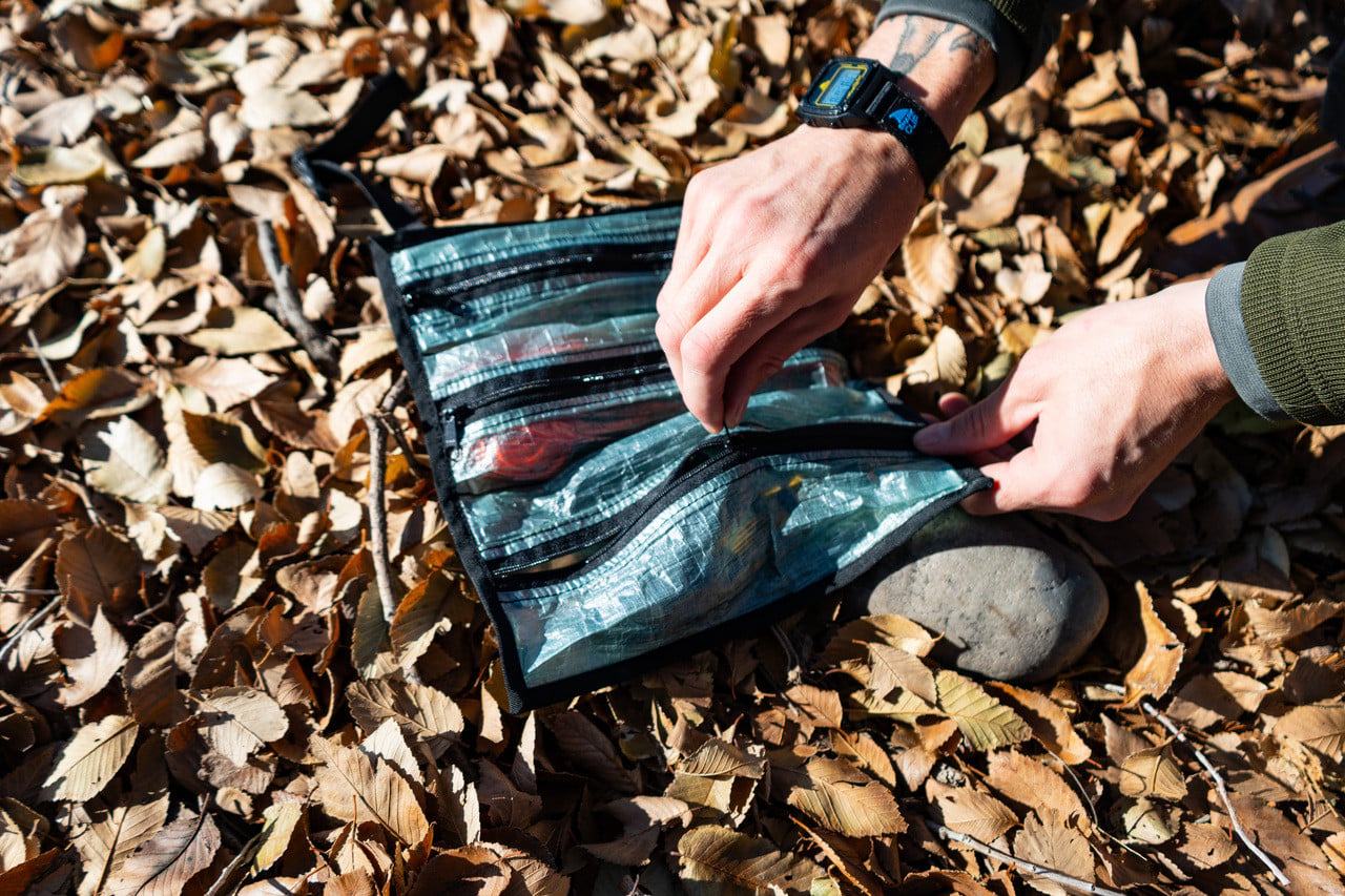 a man zips up a dyneema flat roll, the flatroll is on the ground in leaves