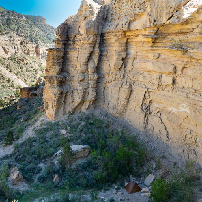 wide view photo of a steep, rocky canyon with a silex tent set up in the valley
