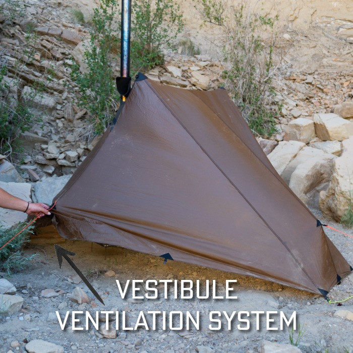man opening back vent on a silex tent set up in a rocky campsite
