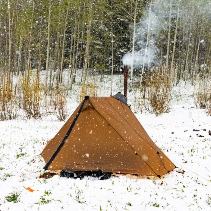 Brown Silex tent with smoke curling out of the stove pipe chimney in a snowy winter forest