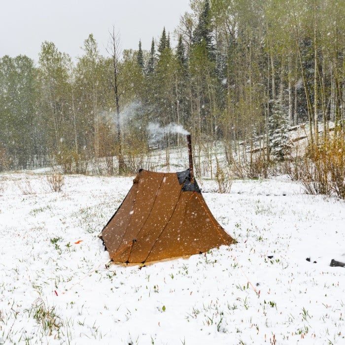 silex tent set up in a snowy meadow, smoke curls from the chimeny of the stove inside the tent