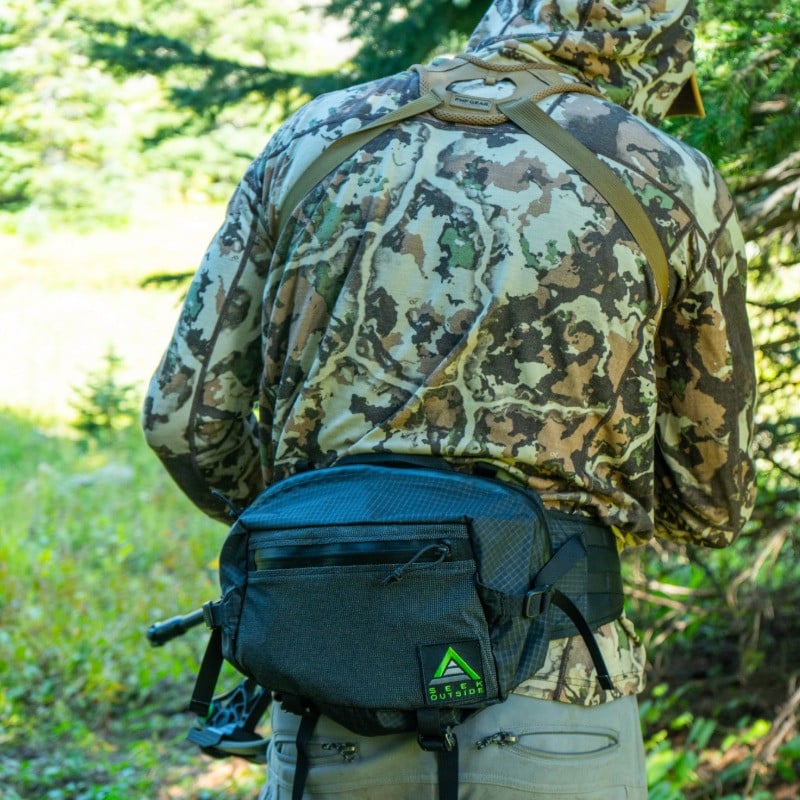 Man in camo shirt wearing a black mesa hip pack in a wooded area, showing the hip pack can carry
