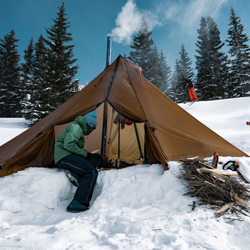 12 person tipi tent staked in deep snow, fire burning inside and gear hanging to dry inside 260 square foot interior