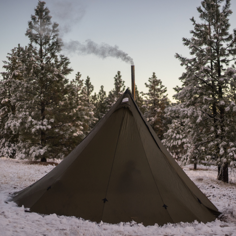 Sunny day at backcountry tipi camp with stove pipe visible and gear tracks in snow around the 13-foot diameter shelter
