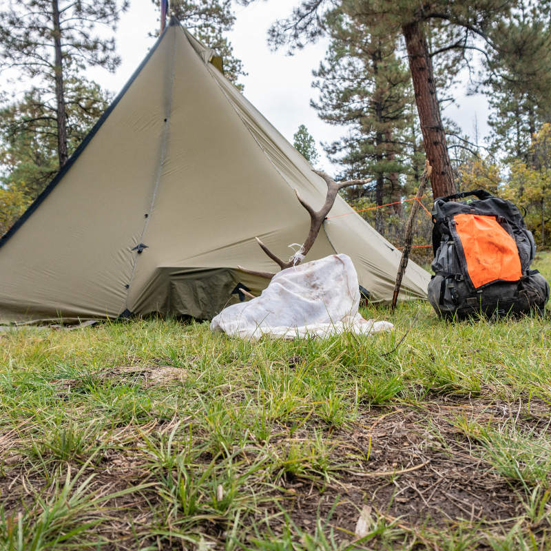 hunting backpack and gear on the ground outside 8 person tipi tent, backcountry basecamp set up 