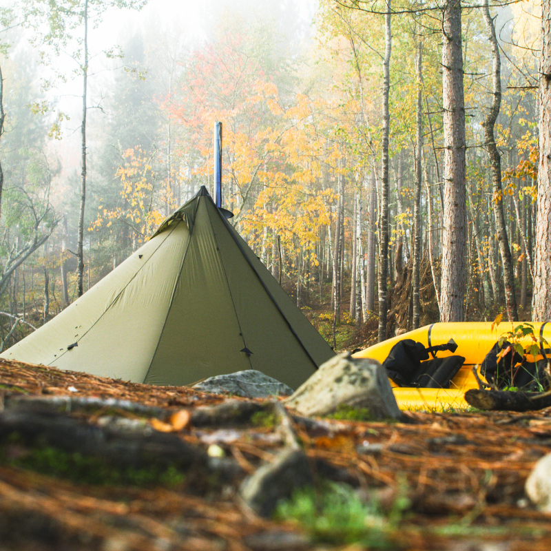 Seek Outside Redcliff hot tent pitched in a wet autumn forest showing angular panels shedding water and 6-inch sod skirt sealing out drafts