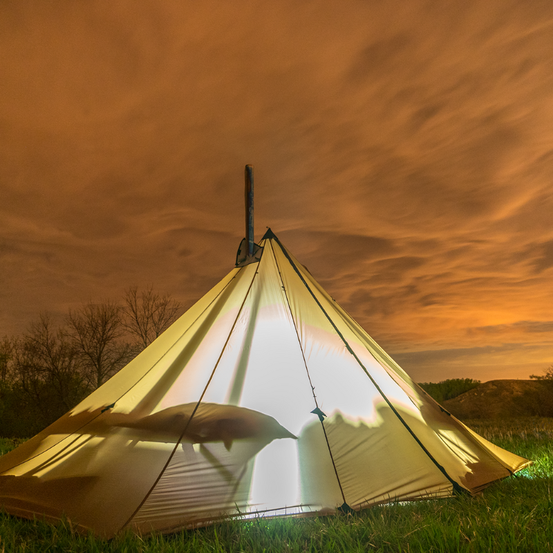 Redcliff hot tent glowing at night with warm light from cots visible through silnylon canopy