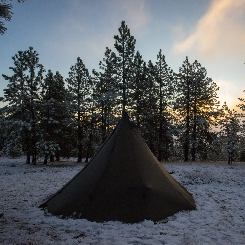 Sunny morning at backcountry tipi camp with stove pipe visible and gear tracks in snow around the 13-foot diameter shelter