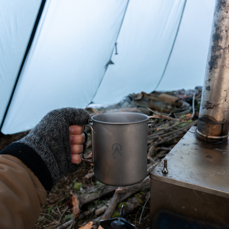 Hot coffee in Seek Outside titanium mug with bail handle held over stove
