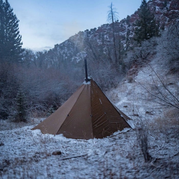 Redcliff light single door shelter in a snowstorm with snow piled up around edges of the tent, and smoke coming from the stove pipe