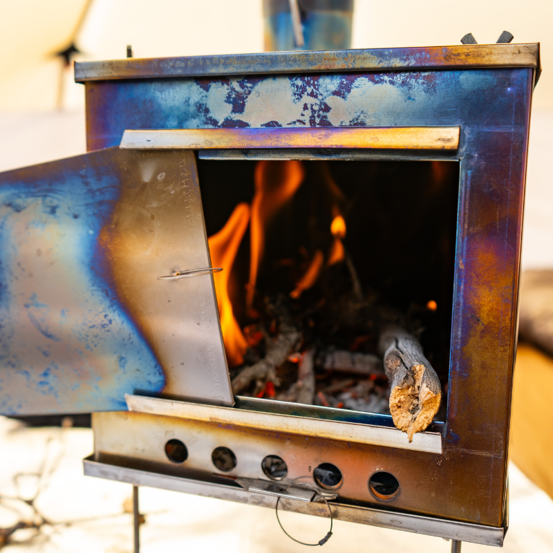 Titanium wood stove with firebox glowing from active fire and heat radiating from titanium panels