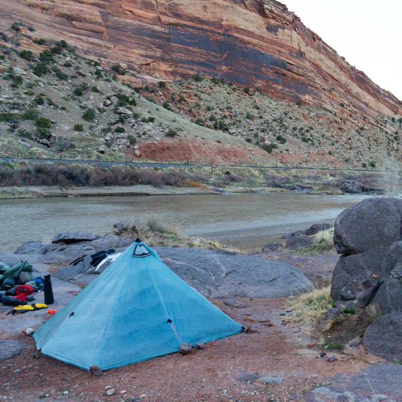 Backpacking tent set up on riverbank canopy fully staked and guy lines tensioned