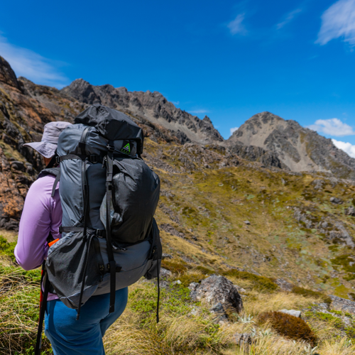 Hiker carrying Seek Outside Unaweep 4800 backpack on trail, 79-liter capacity, top lid and talon added for extra capacity 