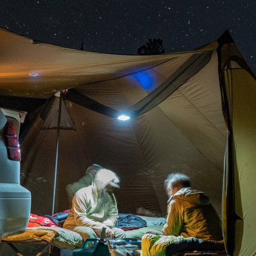 tow men sit on cots inside a bookcliff tent, the nightime scene is illuminated by a light inside the bookcliff attic hanging from the middle of the tent