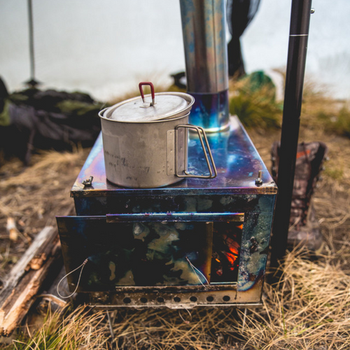 Backcountry cooking on flat top titanium wood stove with fire burning and stovepipe installed