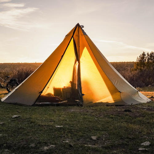 12 person tent set up with sunset light glowing through open doors and baren dirt foreground