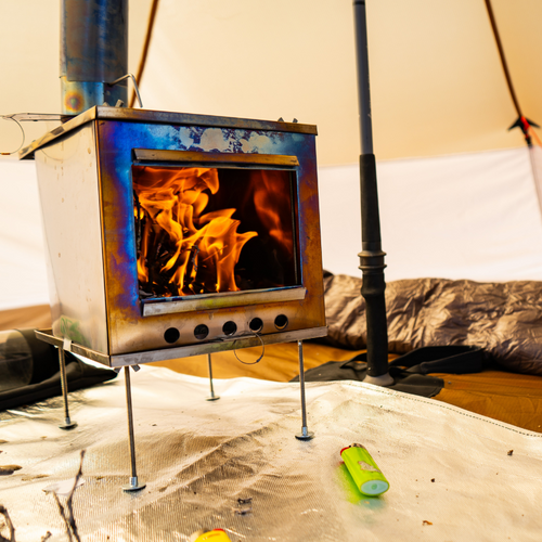 Seek Outside stove with bright orange flames inside and smoke venting through stovepipe