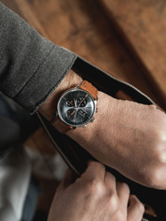 The Junghans Meister Chronoscope 27/4224.03 is a wristwatch that features a stainless steel case, a fixed stainless steel bezel, and a sapphire grey dial with sunray brush and index markers. It has a German automatic movement with hours, minutes, seconds, day, date, stop function, and power reserve functions, a sapphire crystal, a brown leather strap with stainless steel pin buckle, and an exhibition caseback. It is also water resistant and has a chronograph.