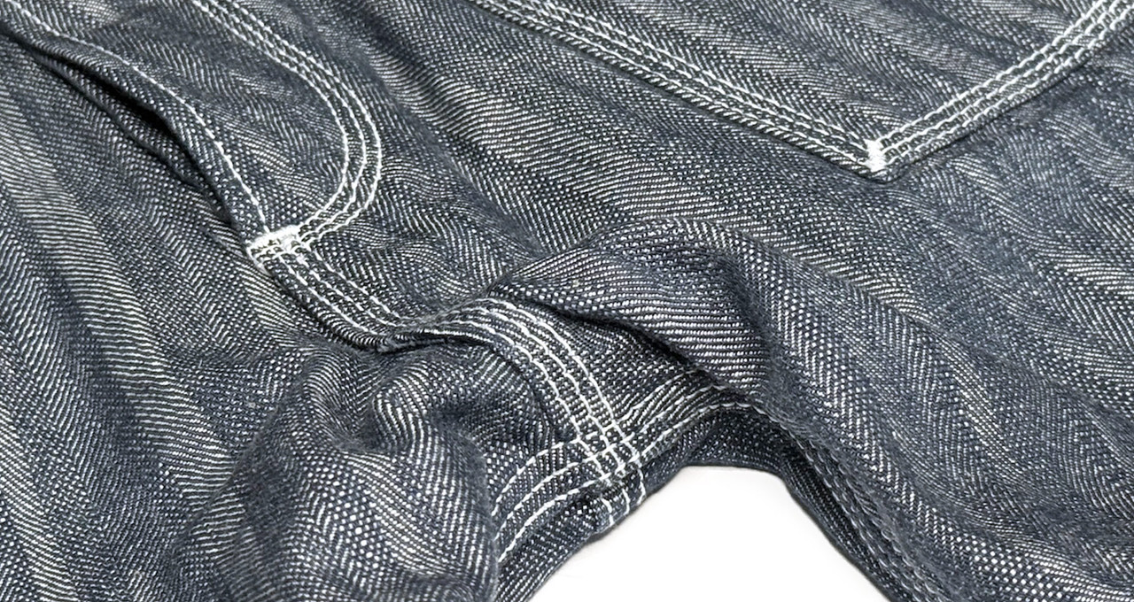 Front close-up detail of the herringbone denim and triple-needle stitch sewing of Williamsburg Garment Company’s customizable men's and women’s work denim pants. The pants are crafted from lightweight 11 oz. cotton herringbone denim and are built for dura