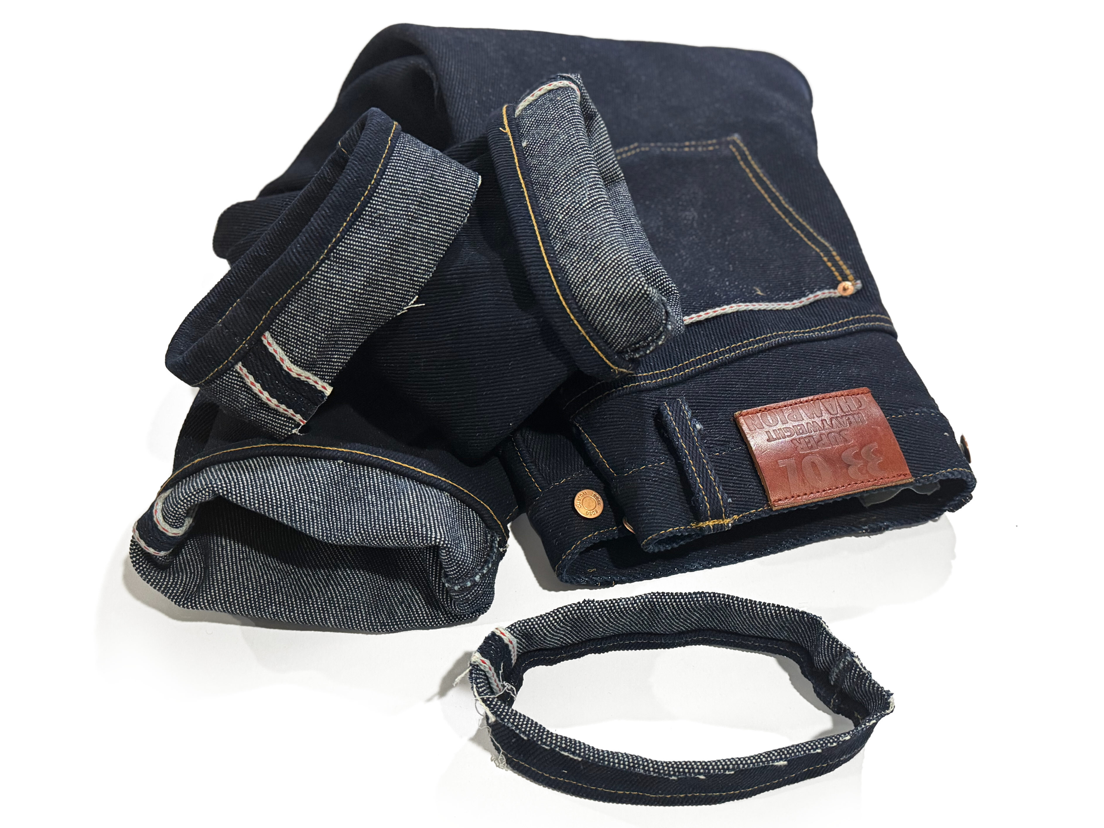 Feature image of heavyweight 33 oz SoSo denim jeans after professional chain stitch hemming at Williamsburg Garment Company. The photo shows the jeans neatly folded with the removed hem ring placed in front, emphasizing the thickness and rigidity of the fabric. Demonstrates our ability to handle extreme heavyweight selvedge denim using our custom-built Union Special 56300.