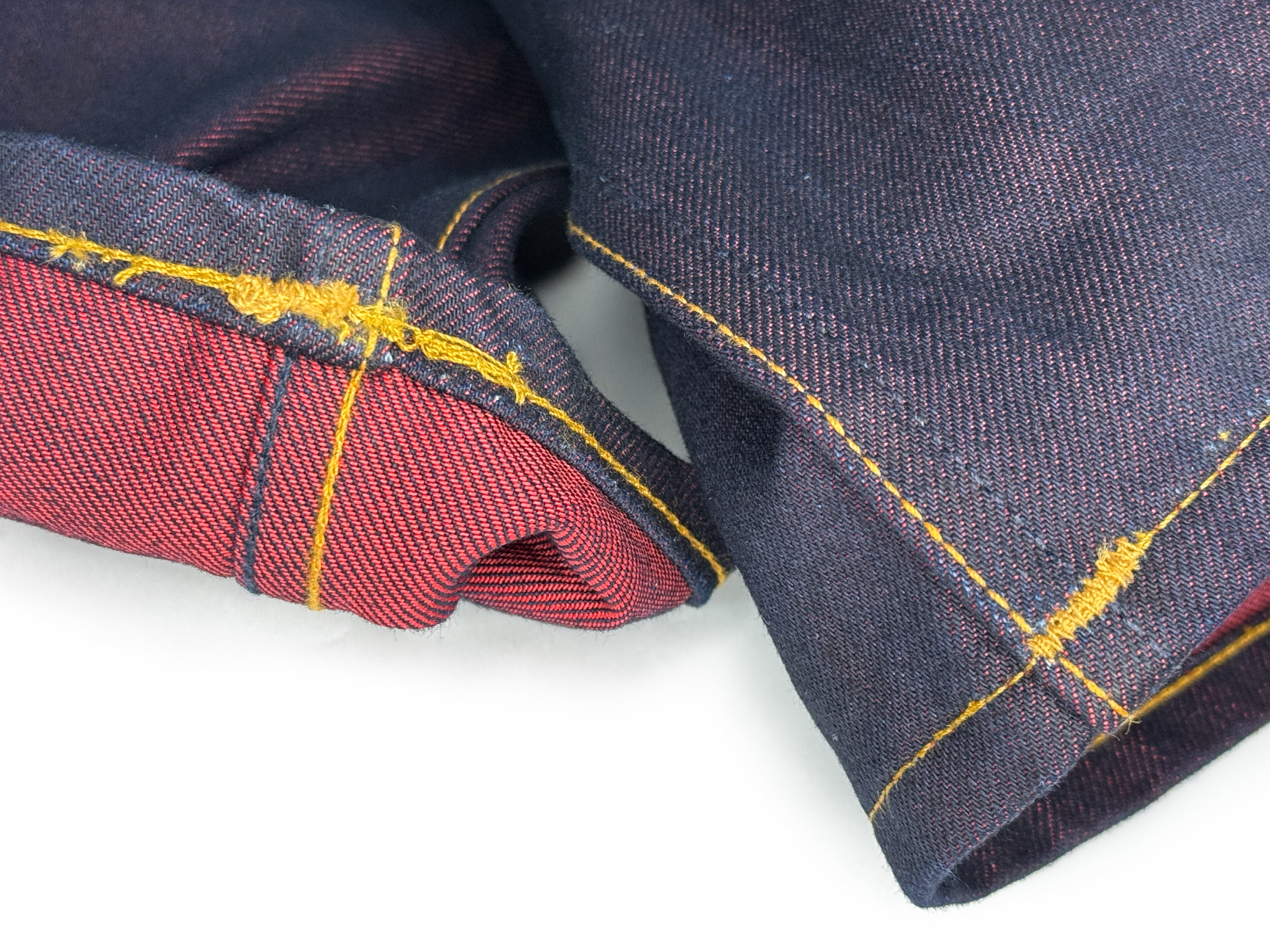 Before example of  poorly executed chain-stitch hemming and bar tacking on red-weft Gustin jeans close-up.