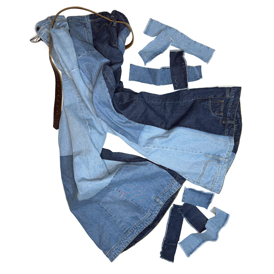 Side-view image of A.W.A.K.E. Mode patchwork jeans after hemming, shown with the cut-away denim sections placed beside the garment to highlight the precision tailoring done at Williamsburg Garment Company.