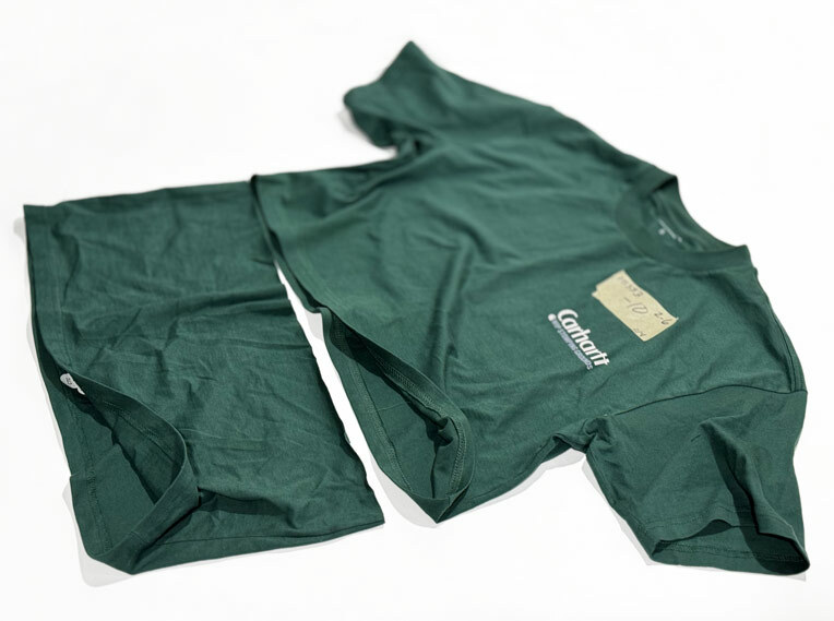 Before and after view of a men's green Carhartt t-shirt customized into a women's cropped t-shirt. The original hem is visible beside the cropped version, highlighting the factory-level sewing on the inside of the garment.