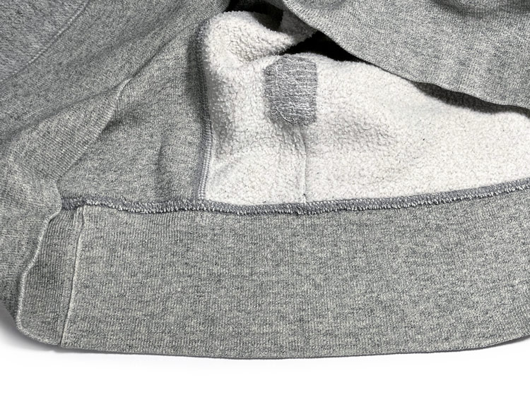 Close-up view of a repaired hole in a fleece hoodie with a fabric patch and mending stitching by Williamsburg Garment Company